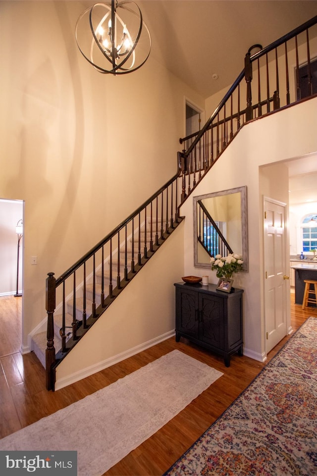 staircase with a chandelier, wood finished floors, a towering ceiling, and baseboards