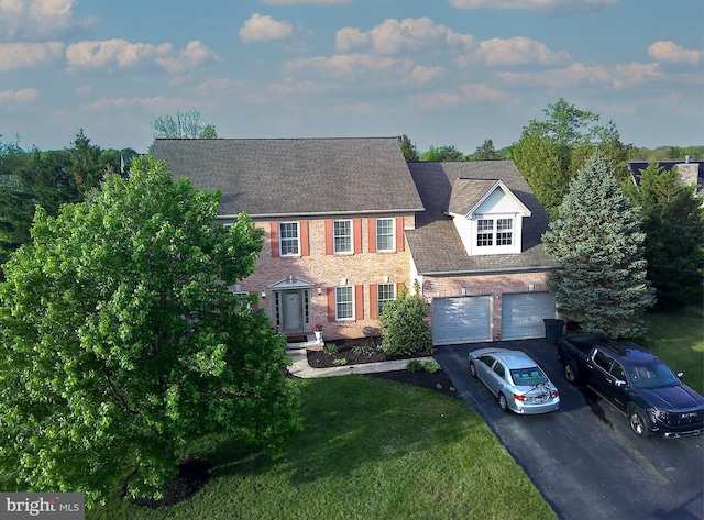 colonial inspired home featuring asphalt driveway, a front yard, an attached garage, brick siding, and roof with shingles