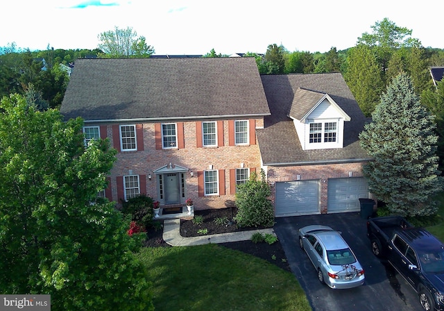 colonial-style house with asphalt driveway, brick siding, and a shingled roof