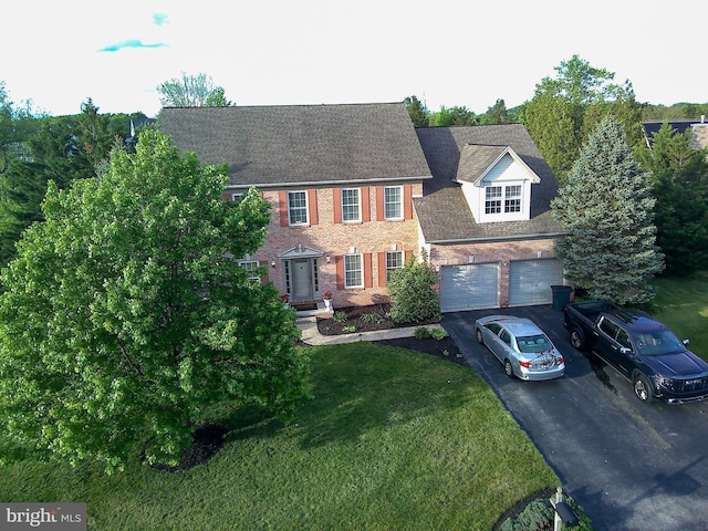 colonial inspired home with driveway, a front lawn, an attached garage, brick siding, and roof with shingles