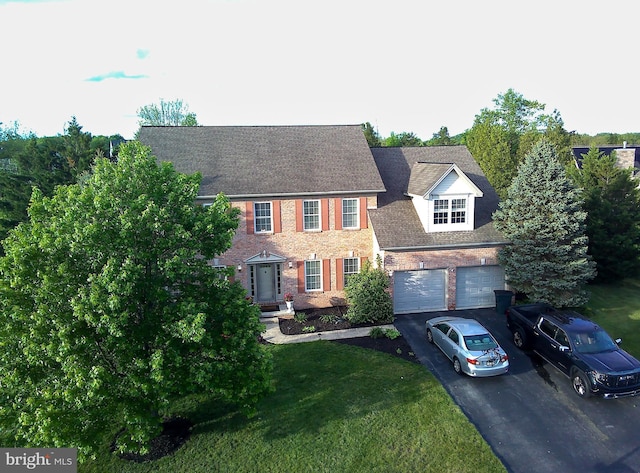 colonial inspired home featuring driveway, a front yard, brick siding, a garage, and a shingled roof