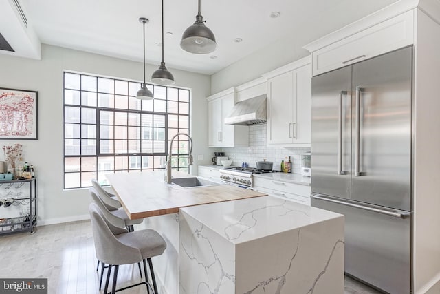 kitchen with premium appliances, a sink, wall chimney exhaust hood, white cabinetry, and backsplash