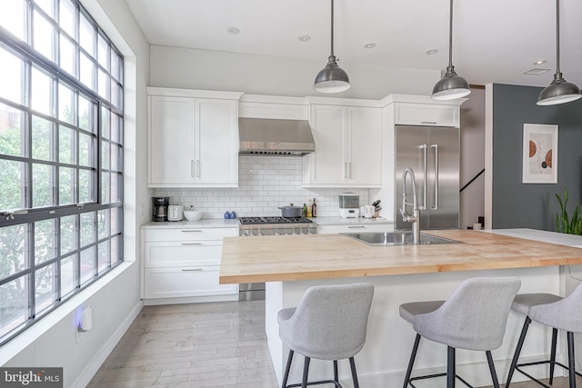 kitchen with wooden counters, stainless steel appliances, wall chimney exhaust hood, a sink, and healthy amount of natural light