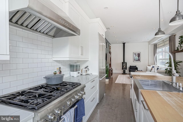 kitchen with wall chimney exhaust hood, butcher block counters, high quality appliances, open floor plan, and white cabinetry
