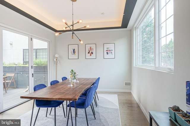 dining room featuring a raised ceiling, a chandelier, wood finished floors, and baseboards
