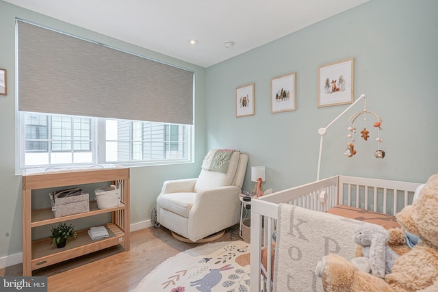 bedroom with wood finished floors, a nursery area, baseboards, and recessed lighting