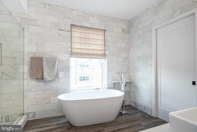 full bathroom featuring tile walls, wood finished floors, and a freestanding tub