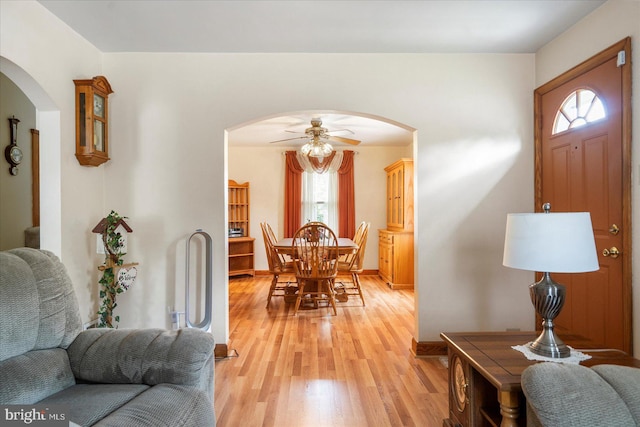 dining room featuring arched walkways, light wood-type flooring, a ceiling fan, and baseboards
