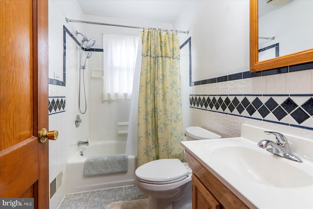 full bath featuring tile walls, shower / bathtub combination with curtain, toilet, vanity, and a wainscoted wall