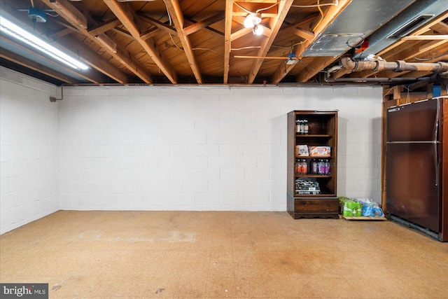 unfinished basement with tile patterned floors and freestanding refrigerator