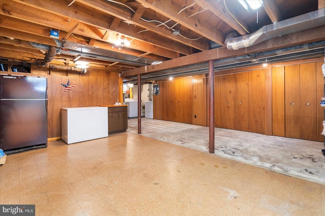 unfinished below grade area with freestanding refrigerator, refrigerator, tile patterned floors, and wood walls