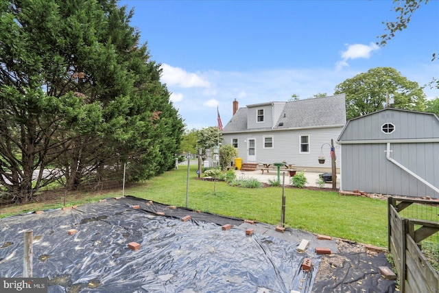 rear view of property featuring a lawn, a shed, a chimney, an outbuilding, and a patio
