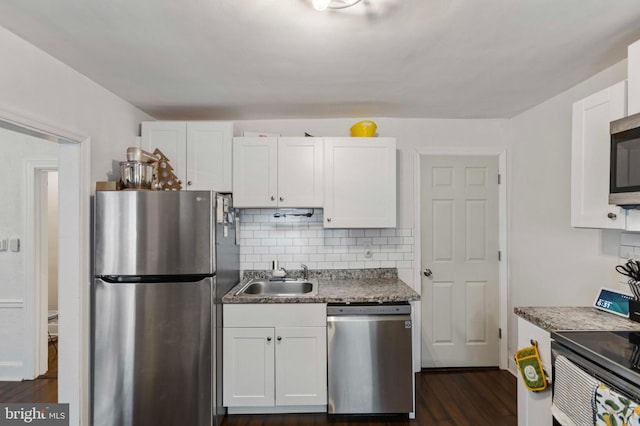 kitchen with stainless steel appliances, a sink, white cabinetry, backsplash, and dark wood-style floors