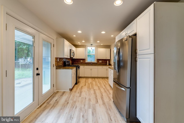 kitchen with stainless steel appliances, a sink, white cabinets, light wood finished floors, and tasteful backsplash