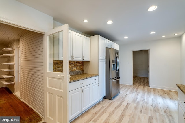 kitchen featuring stainless steel fridge with ice dispenser, light stone countertops, white cabinetry, light wood finished floors, and baseboards