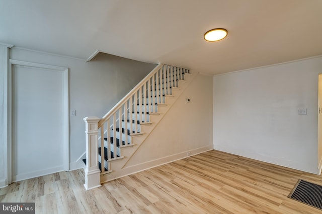 stairs with wood finished floors, ornamental molding, and baseboards