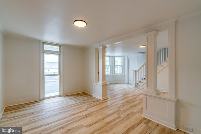 unfurnished room featuring decorative columns, light wood-type flooring, crown molding, stairway, and baseboards