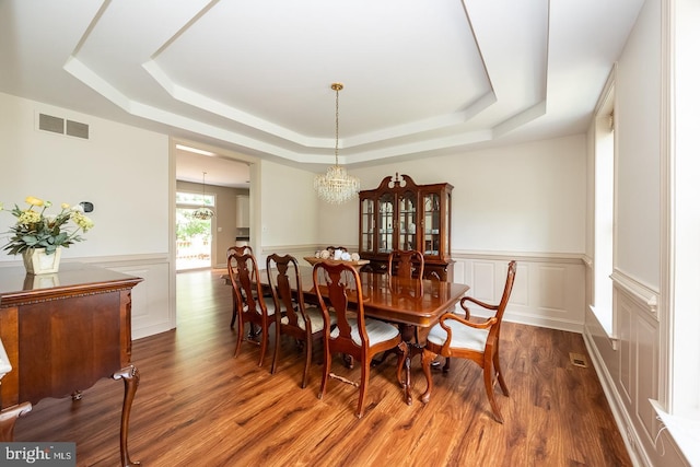 dining space with a tray ceiling, wainscoting, a chandelier, wood finished floors, and a decorative wall
