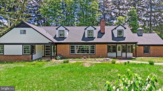 new england style home featuring a chimney, brick siding, a shingled roof, and a front lawn