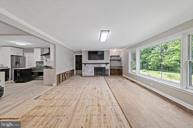 unfurnished living room featuring light wood finished floors, a fireplace, ornamental molding, and baseboards