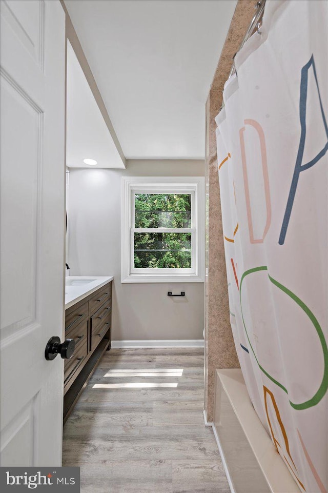 full bathroom with wood finished floors, vanity, baseboards, and shower / tub combo