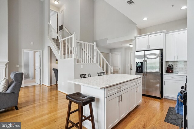 12001 Market St Unit 441, Reston, VA 20190 - kitchen featuring stainless steel fridge with ice dispenser, a high ceiling, white cabinets, light wood finished floors, and a center island