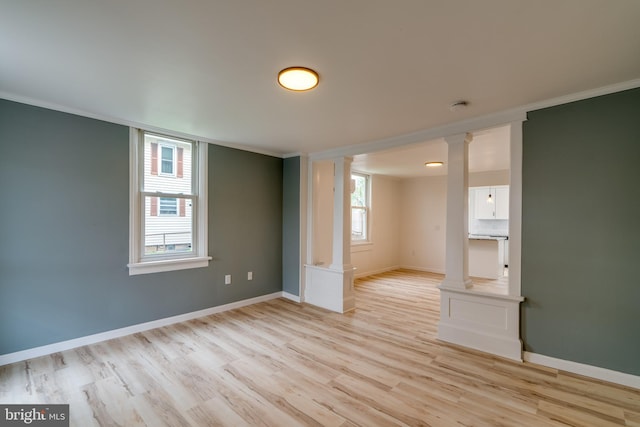 empty room featuring ornate columns, light wood finished floors, baseboards, crown molding, and a smoke detector