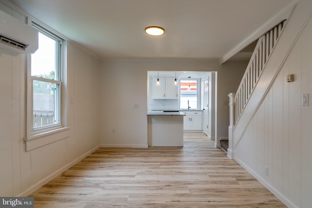 unfurnished living room with a wall mounted AC, light wood finished floors, stairway, ornamental molding, and baseboards