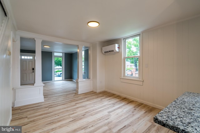 empty room featuring light wood-type flooring, ornate columns, a wall unit AC, baseboards, and crown molding