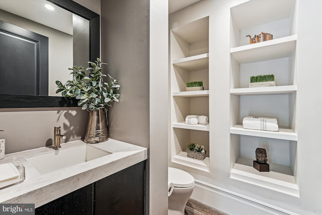 half bathroom with built in shelves, toilet, vanity, and wood finished floors
