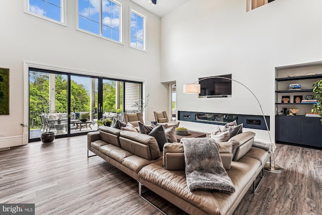 living area featuring a high ceiling, plenty of natural light, wood finished floors, a glass covered fireplace, and baseboards