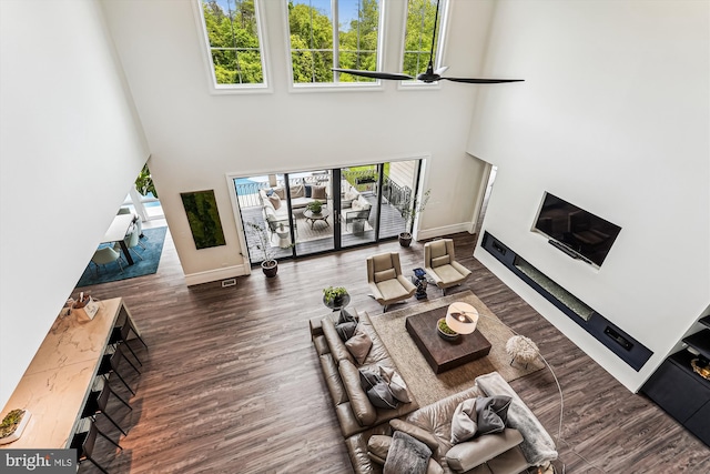 living room featuring a towering ceiling, wood finished floors, ceiling fan, and baseboards