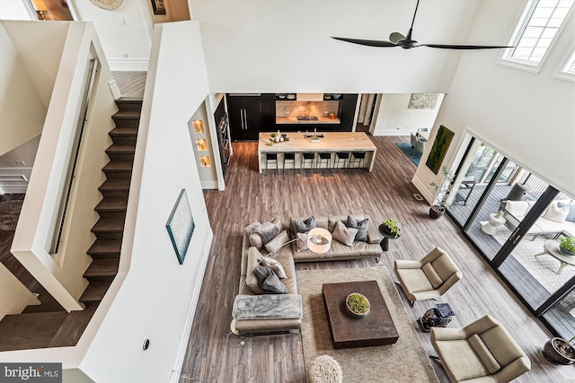 living room featuring stairway, a high ceiling, ceiling fan, baseboards, and wood finished floors