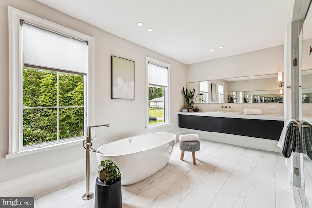bathroom with a freestanding tub, marble look tiles, recessed lighting, and vanity