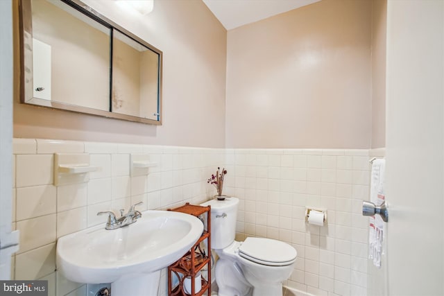 half bathroom featuring a sink, toilet, tile walls, and a wainscoted wall