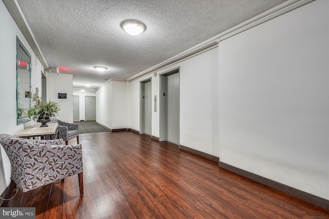 hallway with wood finished floors, a textured ceiling, elevator, baseboards, and crown molding