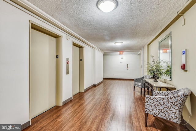 hall with a textured ceiling, wood finished floors, and elevator