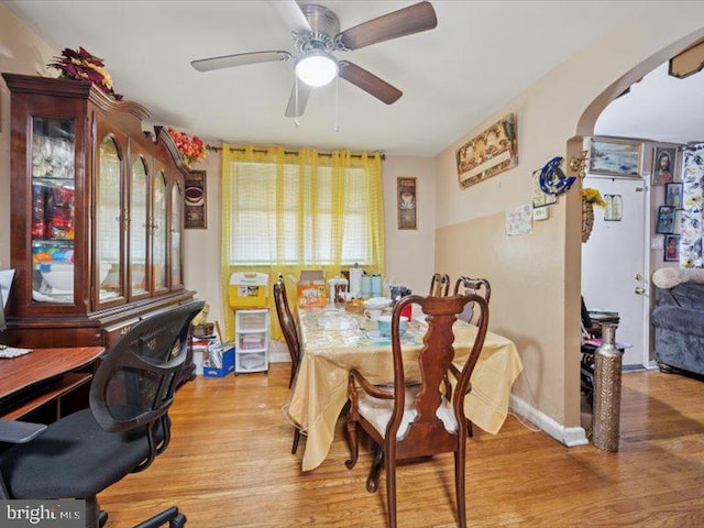 dining room featuring light wood-type flooring, ceiling fan, arched walkways, and baseboards