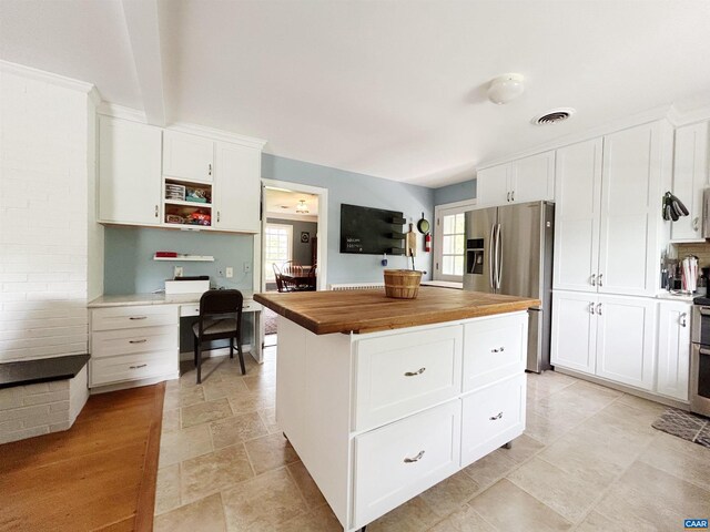 kitchen with wood counters, stainless steel refrigerator with ice dispenser, white cabinetry, a center island, and stone finish flooring