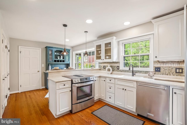 kitchen with stainless steel appliances, a sink, a peninsula, decorative backsplash, and glass insert cabinets