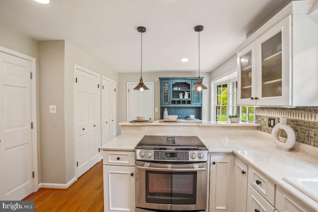 kitchen with stainless steel range with electric cooktop, a peninsula, light wood-style flooring, glass insert cabinets, and decorative light fixtures