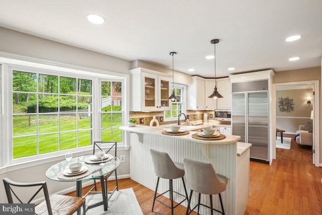 kitchen featuring appliances with stainless steel finishes, a peninsula, glass insert cabinets, light countertops, and white cabinets