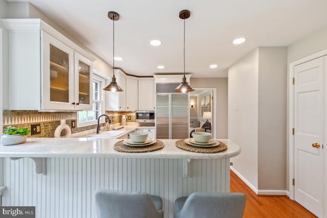 kitchen with a sink, stainless steel appliances, decorative backsplash, light wood finished floors, and recessed lighting
