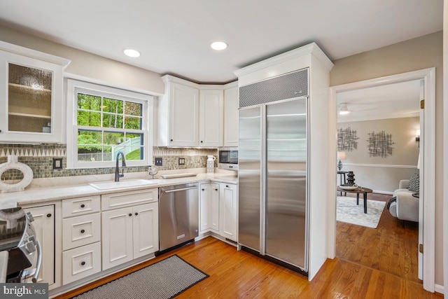 kitchen with appliances with stainless steel finishes, a sink, white cabinetry, decorative backsplash, and light wood-type flooring