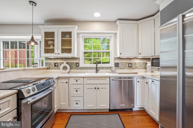 kitchen featuring stainless steel appliances, a sink, white cabinets, backsplash, and wood finished floors
