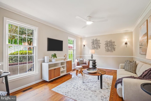 living room featuring ornamental molding, light wood-type flooring, a ceiling fan, and baseboards