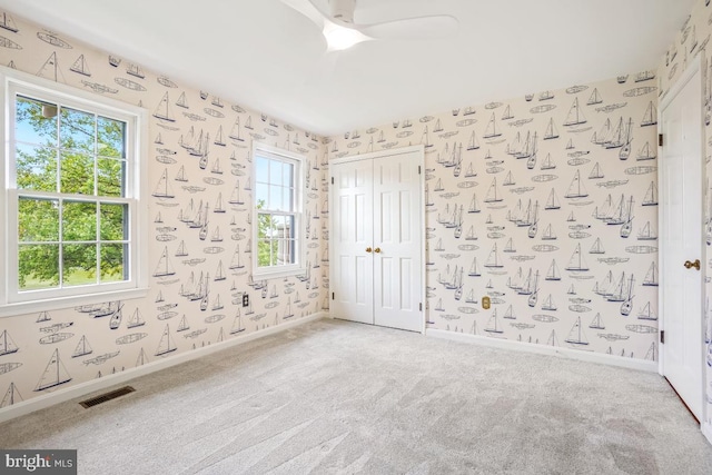 empty room featuring wallpapered walls, carpet, baseboards, and a ceiling fan