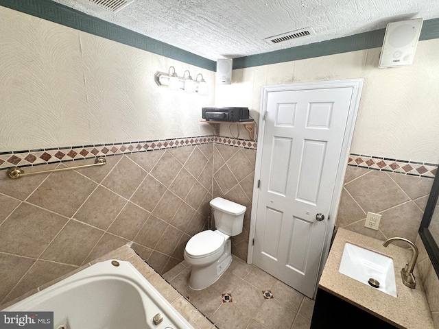 bathroom featuring tile walls, tile patterned floors, a jetted tub, toilet, and a wainscoted wall