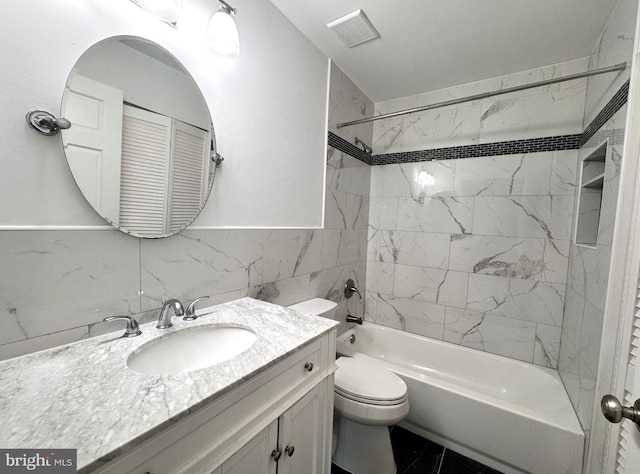 bathroom with toilet, vanity, tile walls, tub / shower combination, and a wainscoted wall