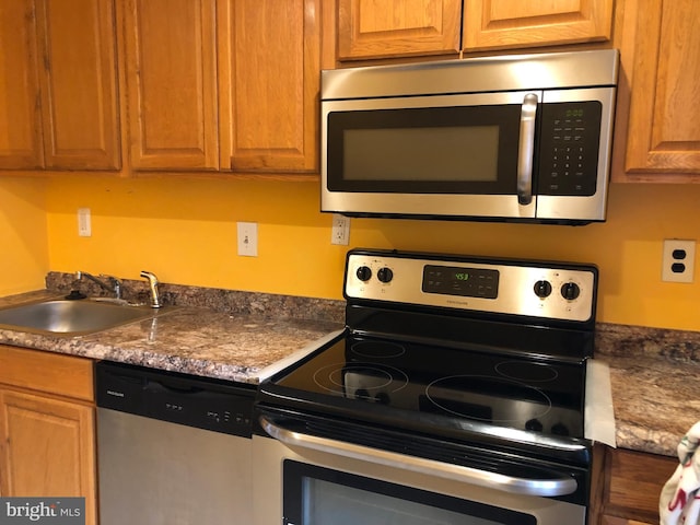 kitchen with appliances with stainless steel finishes, a sink, and brown cabinetry